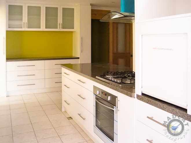 Completed kitchen with white cabinetry, an olive glass splashback and a stone-topped island, Beldon job